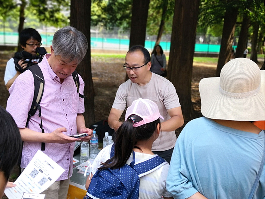 みま~もいたばしのイベントで「みまもりあい」アプリの説明をする水野さん(写真中央)=清川卓史撮影