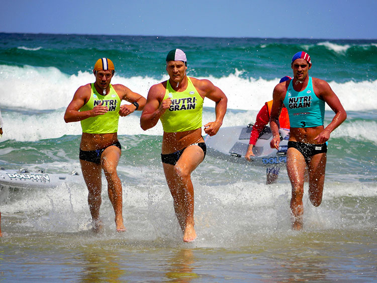 鉄人レースでボードから砂浜に上陸。サーフスキーに切り替わるまでの距離を男性選手たちが駆け抜ける=小暮哲夫撮影