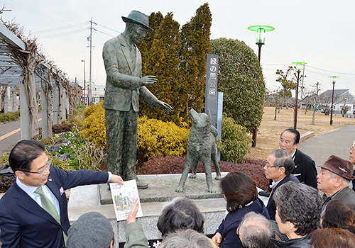 上野博士とハチ公の像を訪れ、前葉泰幸・津市長(左端)から説明を受ける秋田県大館市の関係者=三重県津市の久居駅前