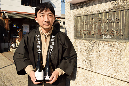 「ねこ正宗」を手に正門前に立つ今宿さん=滋賀県東近江市八日市上之町