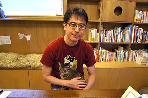 「Cat’s Meow Books(キャッツミャウブックス)」店主の安村正也さんと抱っこされる「鈴」ちゃん